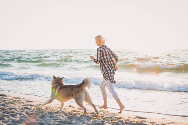 Young female running with siberian husky dog on sea front at sunrise - Photo, image