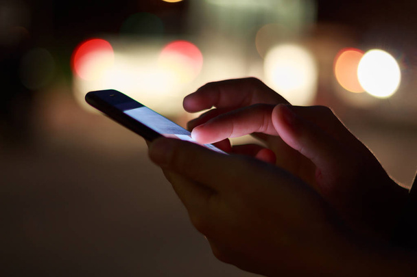 γκρο πλαν χέρι χρησιμοποιώντας το τηλέφωνο τη νύχτα στην οδό - Φωτογραφία, εικόνα