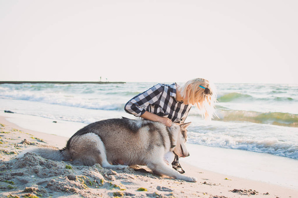 Young female hugging with siberian husky dog on the beach at sunrise - Fotoğraf, Görsel