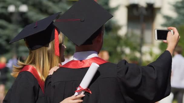 Man en vrouw in academische toga's en caps nemen selfie op graduatie ceremonie - Video