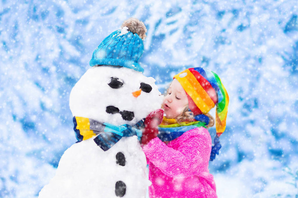 Küçük kız bir kar adam kışın bina - Fotoğraf, Görsel