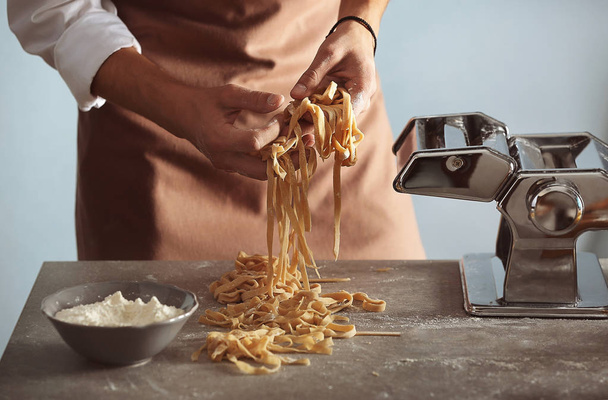 Man preparing pasta on kitchen table, close up view - Foto, imagen