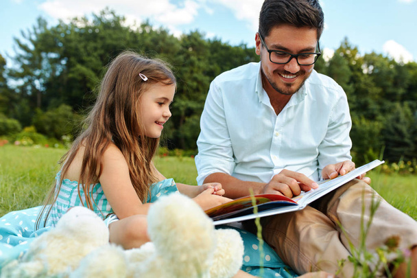Dad Reading Child A Book In Park. Father And Daughter In Nature - Foto, imagen
