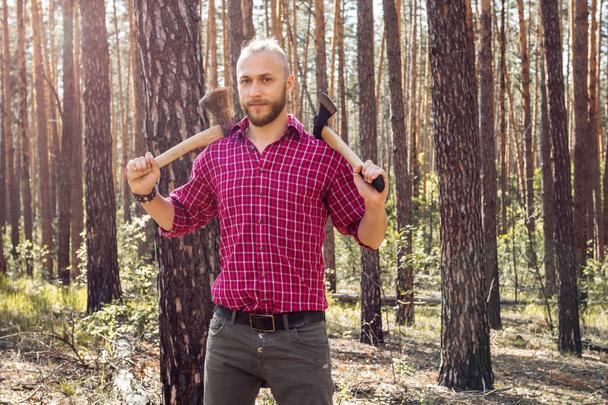 Bearded man with a hatchet in the woods on a background of trees - Valokuva, kuva