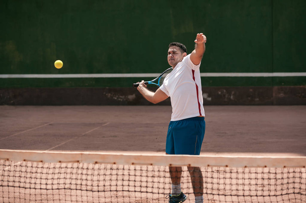 Handsome young man on tennis court. Man playing tennis. Man hitting tennis ball - Valokuva, kuva
