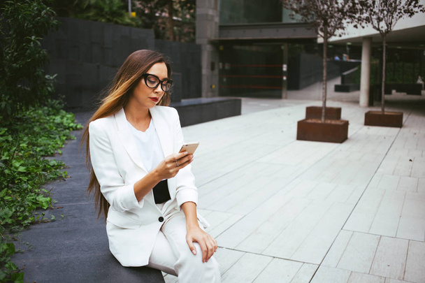 Primer plano retrato de mujer hermosa en traje blanco está sentado al aire libre en un patio trasero y el uso de su teléfono celular
 - Foto, imagen