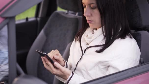 Woman writes a message on a smartphone sitting in the car - Πλάνα, βίντεο