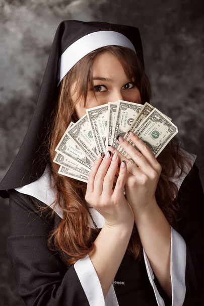 closeup attractive nun with dark hair is holding a dollar bill and covers his face them - Fotoğraf, Görsel