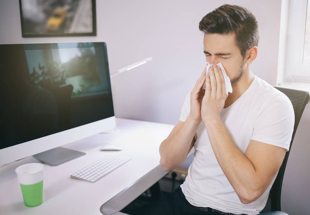 Side view of the patients employer. sneezing into a tissue in an office near the window in the computer. Freelancer designer with  cold - Foto, imagen