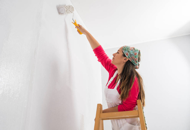 Młoda dziewczyna stoi na drabinie malowania ścian  - Zdjęcie, obraz