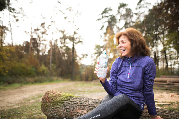 Senior runner sitting on wooden logs, resting, drinking water. - Foto, immagini
