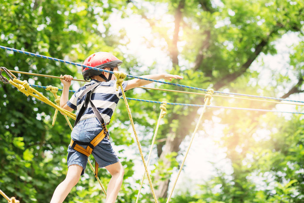 Kids climbing in adventure park. Boy enjoys climbing in the rope - Photo, Image
