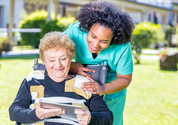 Enfermera explicando uso tableta a anciana en silla de ruedas
 - Foto, Imagen
