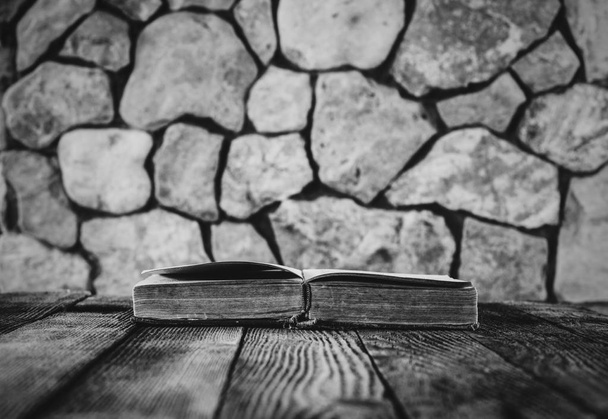 open old book on old wooden table on a background of stone walls. selective focus, black & white photo. with space for your text - 写真・画像