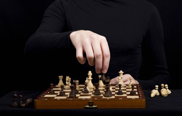 man in een zwarte jas transponeert een pion op een houten schaakbord - Foto, afbeelding