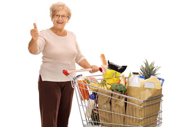 Mature lady with shopping cart giving thumb up - Foto, imagen