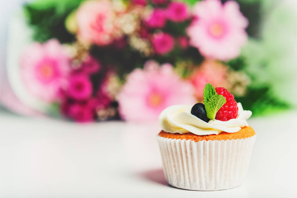A vaj tejszín és a friss bogyós gyümölcsök, a csokor rózsaszín virágok a háttérben egy cupcake - Fotó, kép