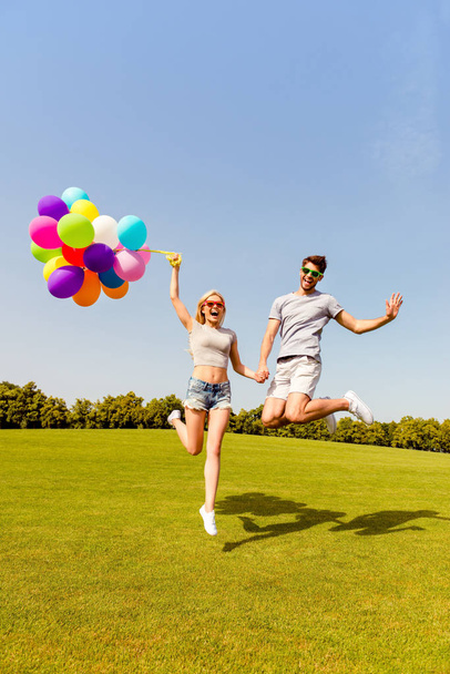 Happy man and woman holding balloons and jumping in the park - Foto, afbeelding
