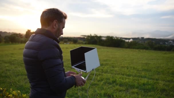  Vousatý muž, oblečený v péřová bunda sledoval jeho tabletu a usmíval se při pilotování dron v polích, selektivní fokus na západ slunce - Záběry, video