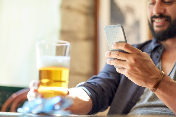 close up of man with smartphone and beer at pub - Foto, Imagen