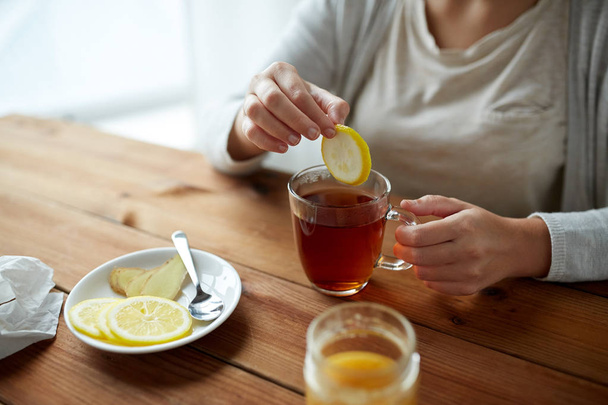 close up of woman adding lemon to tea cup - Foto, afbeelding