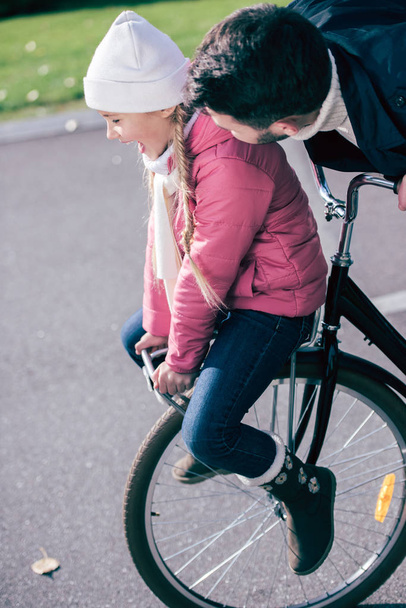 Father carrying smiling daughter on bicycle - Fotoğraf, Görsel