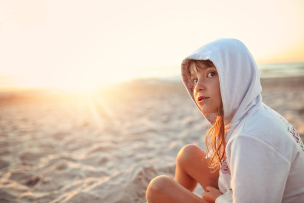 Young girl in the hood sitting on the beach - Foto, afbeelding