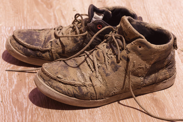 Zapatos sucios con barro seco en el suelo
 - Foto, Imagen