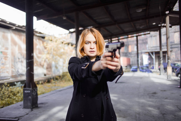 Woman pointing a gun. Mafia girl shooting at someone on the street. - Foto, Imagen