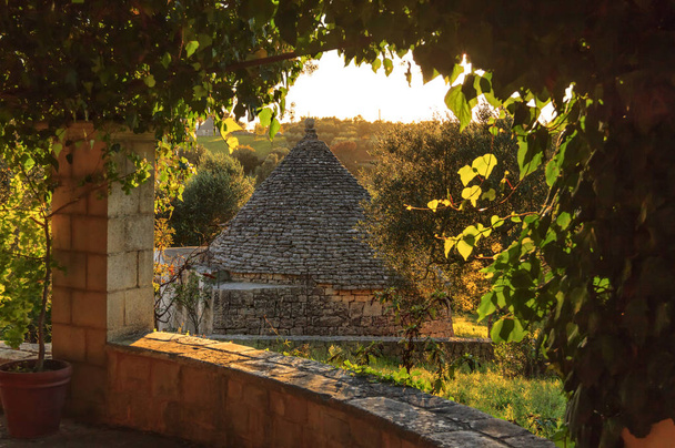 Włochy: Apulia wsi. Valle d'Itria, terytorium Cisternino. Wzgórza z drzewami oliwnymi i Trullo.Typical przykład krajobrazu wiejskiego Apulii. Portyk z widokiem na krajobraz o zachodzie słońca. - Zdjęcie, obraz