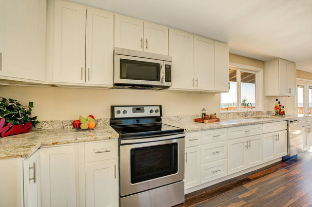 Φωτεινό εσωτερικό της κουζίνας με λευκά γραφεία και μετρητές γρανίτη - Φωτογραφία, εικόνα