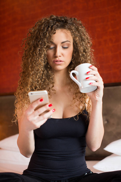 Young woman at home drinking coffee and texting - Фото, изображение