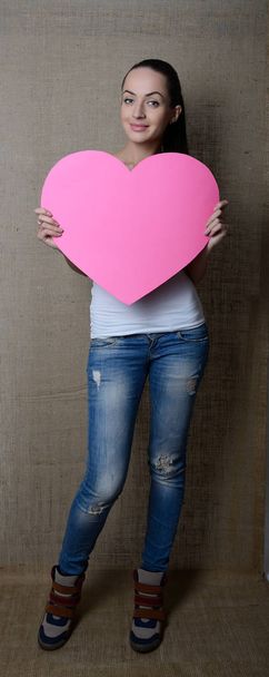 portrait of attractive smiling young woman with pink heart, love holiday valentine symbol over canvas background, toned - Foto, Imagen