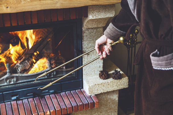 Stoke fireplace. Brass fireplace tongs in hand man - Zdjęcie, obraz