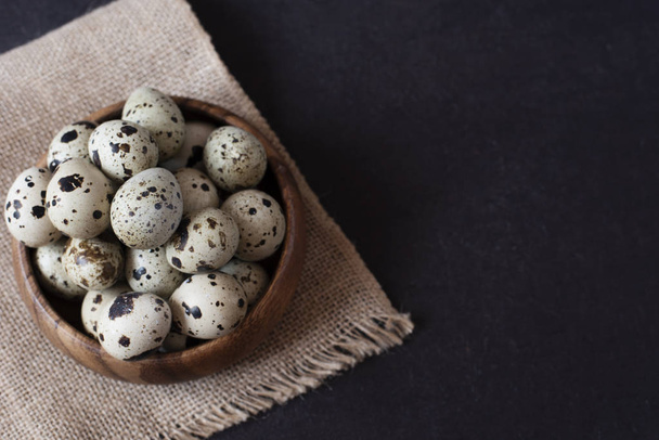 Wooden bowl with quail eggs. Dark food photography. Rustic background, selective focus and diffused natural light. A different type of concept image for Easter. Copy space. - Foto, imagen