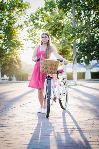 Young woman with city bike going in the park at sunrise or sunset - Photo, image