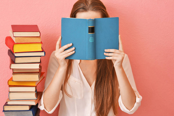 Vrouw zitten op een verdieping en houdt boek voor gezicht op roze achtergrond - Foto, afbeelding