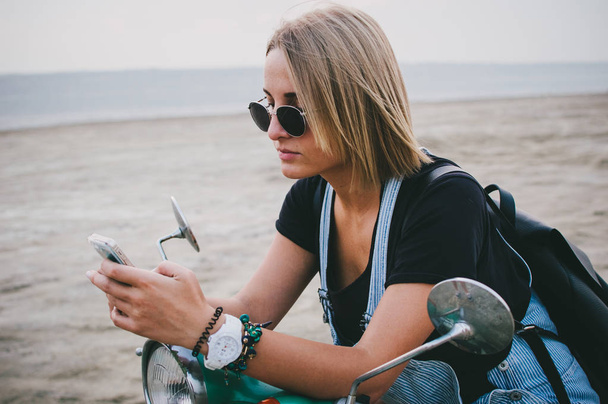 Young woman sitting at vintage scooter and using phone - Photo, image