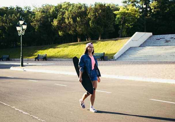 Giovane ragazza con longboard che cammina da sola nel parco all'alba o al tramonto
 - Foto, immagini