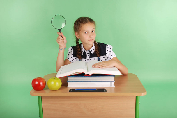 Menina em um uniforme escolar sentado em uma mesa com uma lupa
 - Foto, Imagem