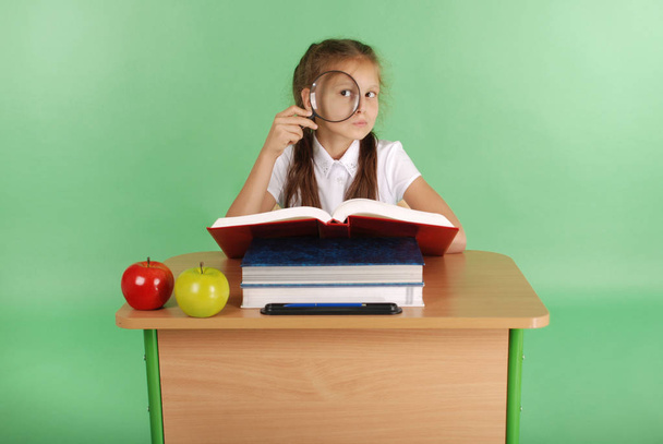 Fille dans un uniforme scolaire assis à un bureau avec une loupe
 - Photo, image