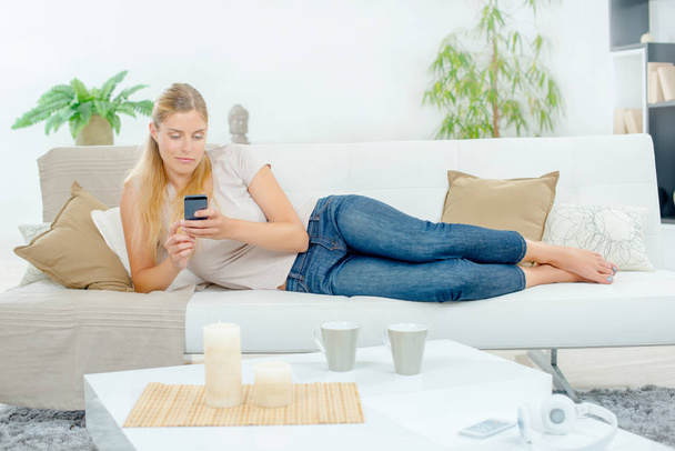 Lady layed on couch, using cellphone - Foto, Imagem