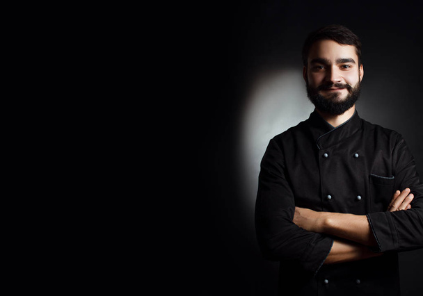 Professional chef with a beard in black uniform on a black background - Photo, Image