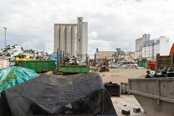 Müllhalde im Hof einer Fabrik mit großem Ofen und Aufbereitungsanlage im Hintergrund mit großen Wolken und Dampf aus Rohren darüber - Foto, Bild