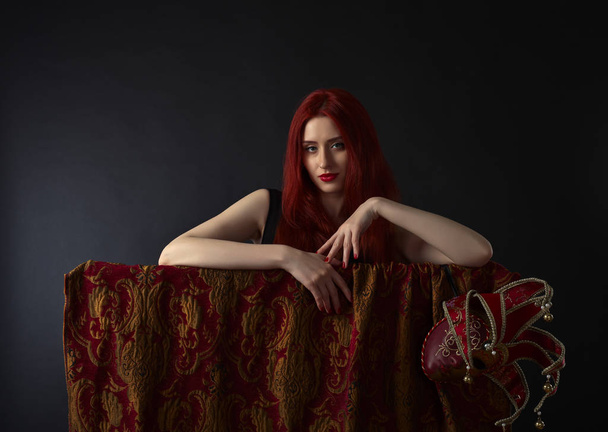 Kaunis punatukkainen nainen, jolla on karnevaalimaski mustalla taustalla
 - Valokuva, kuva