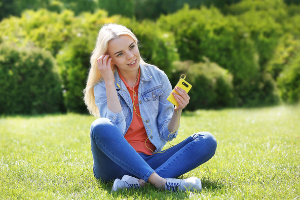 Young beautiful woman with earphones sitting on the grass and listening to music - Фото, изображение