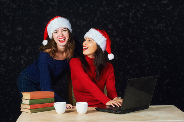 Two young girls in red Christmas hats Santa write letter to Santa - Foto, imagen