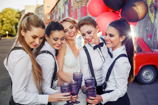 Прекрасные счастливые девушки празднуют девичник и пьют шампанское. Платья подружек невесты в мужских костюмах. Невеста в белом сексуальном платье
. - Фото, изображение