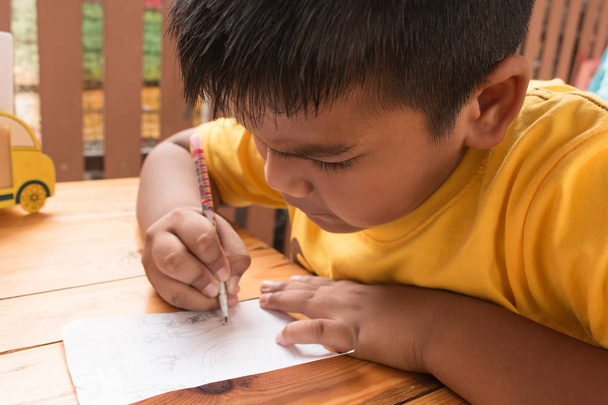 Милый маленький азиатский мальчик делает домашнее задание на столе
  - Фото, изображение
