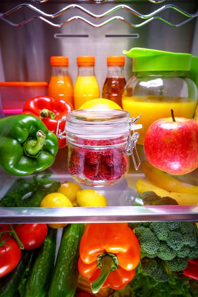 Fresh raspberries in a glass jar on a shelf open refrigerator - Fotó, kép